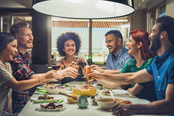 Young cheerful people having fun at dinner party and toasting with alcohol.